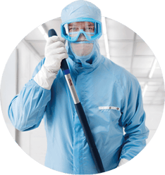 L'image représente un portrait circulaire d'un professionnel portant une combinaison de protection bleue, des lunettes de protection et des gants, et tenant un outil de nettoyage à long manche dans un laboratoire ou une salle blanche. Sous l'image, le titre en gras 