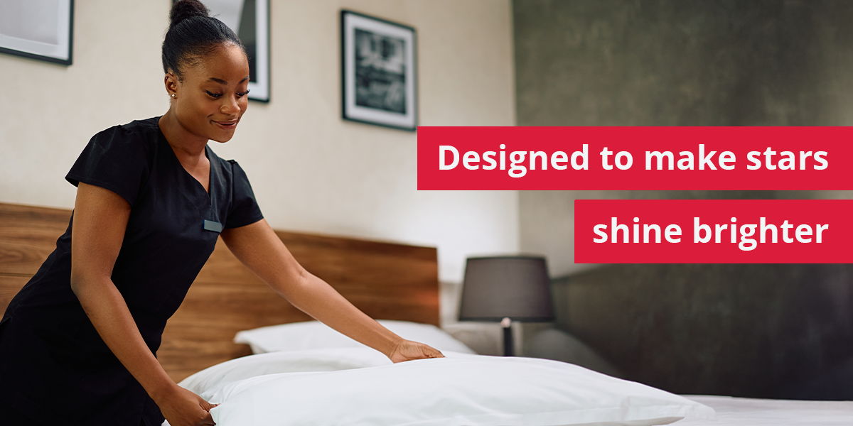 A professional housekeeper in a dark uniform neatly arranges white pillows on a made bed in a modern hotel room. Overlaying the image on the right are two red banners with white text that read, "Designed to make stars shine brighter".