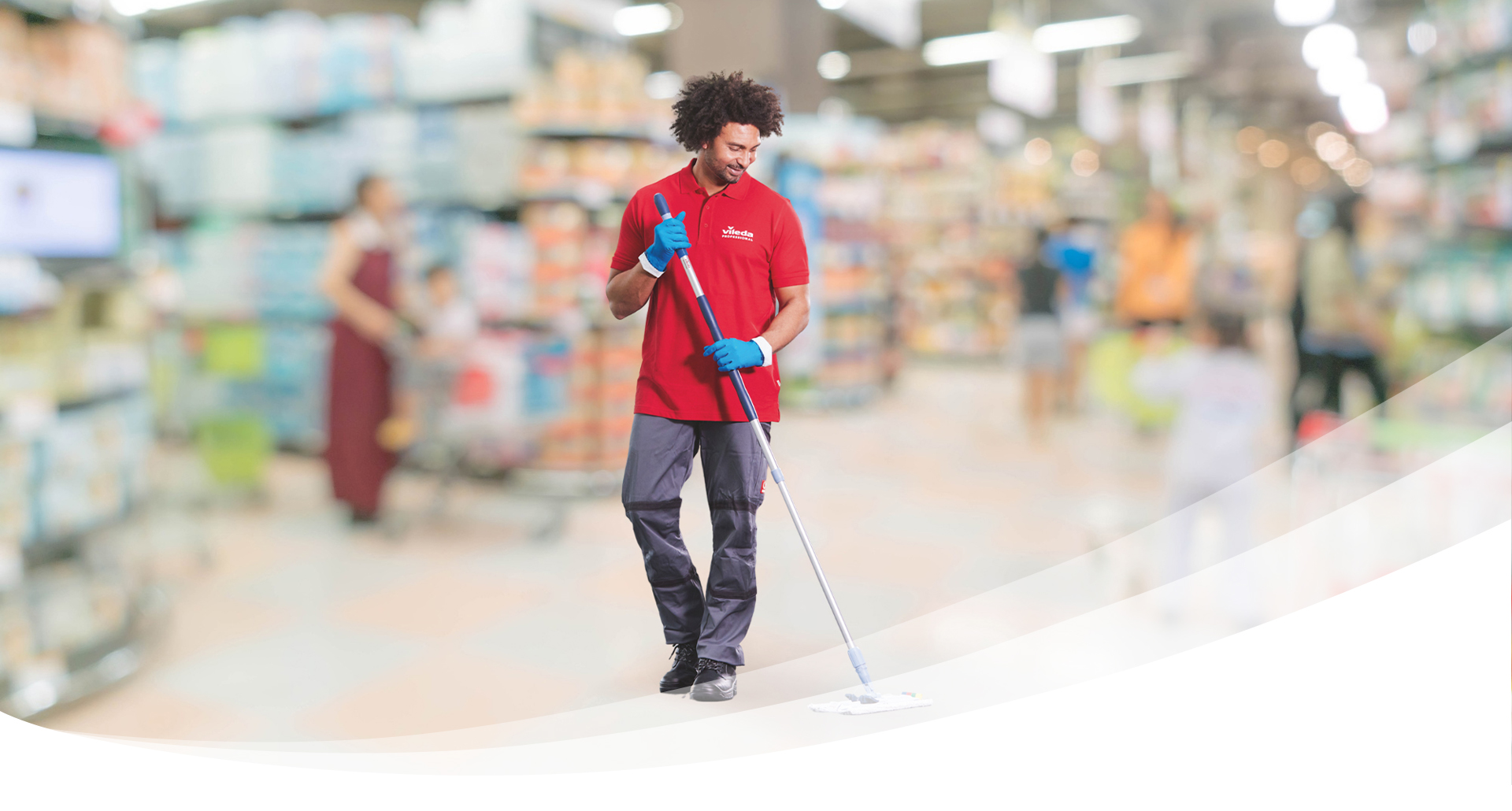 A Vileda Professional cleaner in a red polo shirt and blue gloves mops the floor of a brightly lit, modern grocery store.